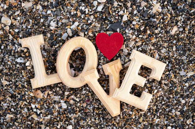 Foto letras de madera que forman la palabra amor con un corazón rojo en un fondo de arena de playa concepto de san valentín