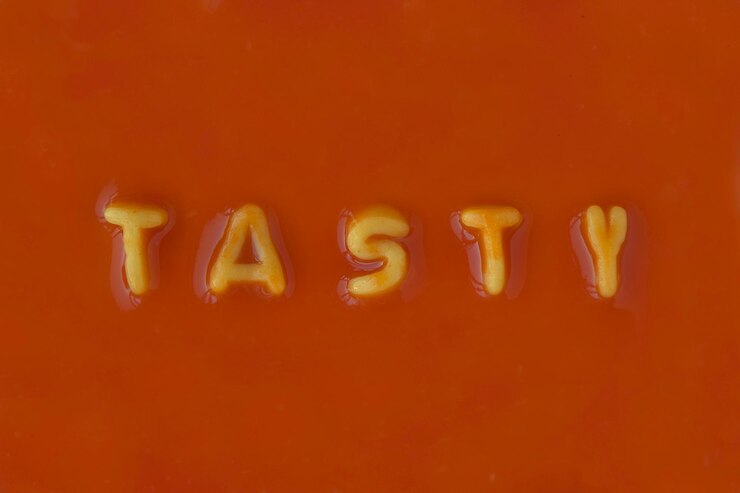 Foto letras de pasta naranja que deletrean la palabra sabrosa en salsa de tomate roja vista desde arriba