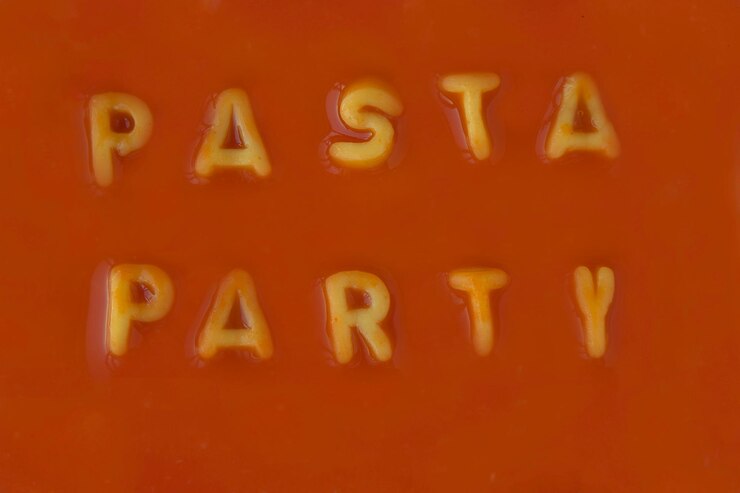 Foto letras de pasta naranja que deletrean las palabras fiesta de pasta en salsa de tomate roja vista desde arriba