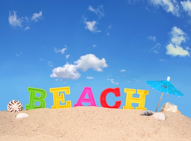 Letras de playa en la arena de una playa contra el cielo azul