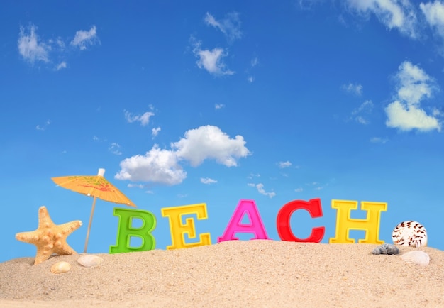 Letras de playa en una arena de playa contra el cielo azul