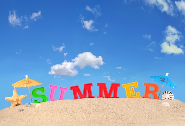 Letras de verano en la arena de una playa contra el cielo azul