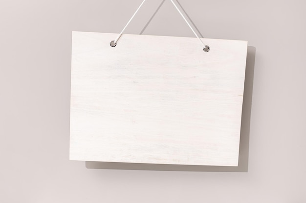 Letrero de madera blanqueada blanca en blanco colgado sobre fondo beige Plantilla simulada