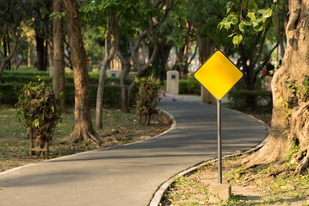 Foto un letrero de metal amarillo vacío al lado de la carretera para correr en el parque público