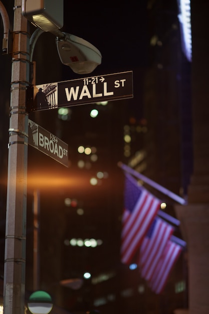 Los letreros de Broadway y Wall Street en la noche con banderas estadounidenses en el fondo, Manhattan, Nueva York