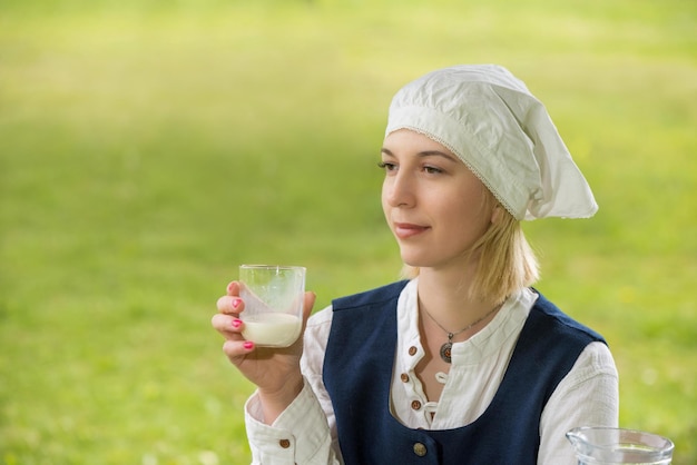 Lettische Frau in traditioneller Kleidung mit Milchglas in der Natur