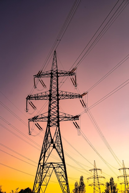 Letzte Strahlen der untergehenden Sonne vor den gigantischen Türmen der Hochspannungsleitungen Dunkler, dünner Rauch über den Türmen der elektrischen Ausrüstung vor dem Hintergrund des rosa und gelben Himmels