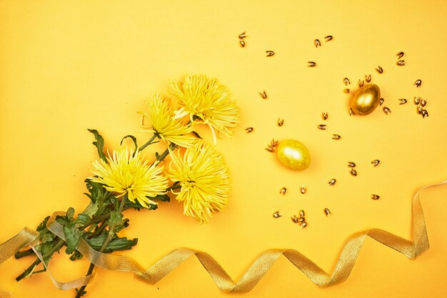 Leuchtend gelbe Frühlingsblumen und goldene Ostereier auf gelbem Hintergrund