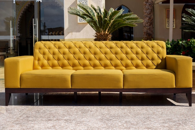 Leuchtend gelbes Sofa steht auf der Außenterrasse auf Palmen-Backgrou