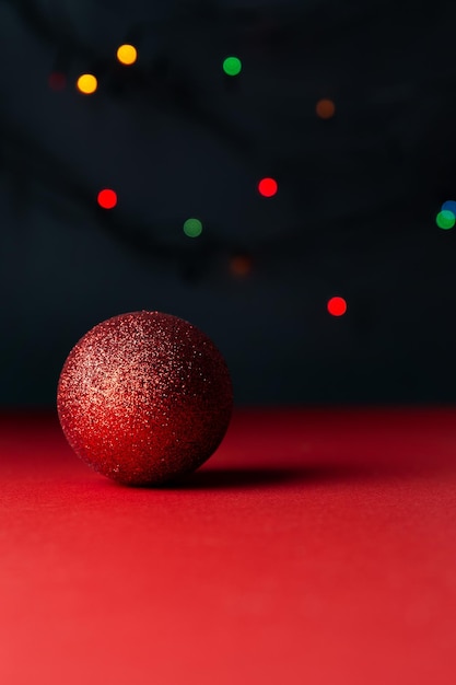 Leuchtend glänzender roter Ball mit schönem Schatten auf rotem Hintergrund mehrfarbiges Bokeh auf schwarzem Weihnachtshintergrund