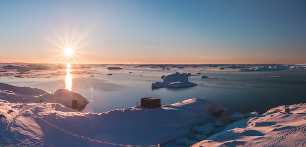 Leuchtend rosa Sonnenuntergang über der Küste der Antarktis und der Station Vernadsky. Erstaunlicher Panoramablick auf die sonnenbeschienene Polarbucht. Die schneebedeckte Oberfläche des Südpols neben der gefrorenen Wasseroberfläche.