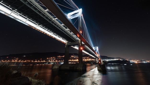 Leuchtende Brücke von unten, die sich nachts im Wasser spiegelt