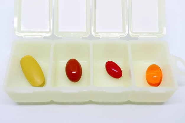 Leuchtende, farblich sortierte Nahrungsergänzungsmittel in einer geöffneten weißen täglichen Pillendose