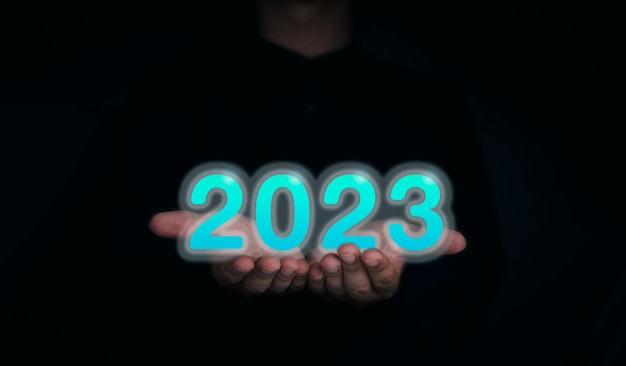 Leuchtender und leuchtend blauer Jahreskalender 2023 Die 2023-Zahlen auf den Händen des Geschäftsmanns auf dunklem Hintergrund für Digital- und Technologiekonzept Willkommen Frohe Weihnachten und Happy New Year Banner