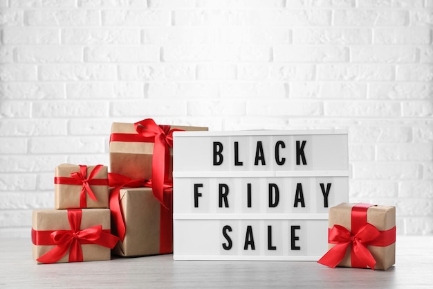 Leuchtkasten mit Worten Black Friday Sale und Geschenkboxen auf Holztisch vor weißer Ziegelwand