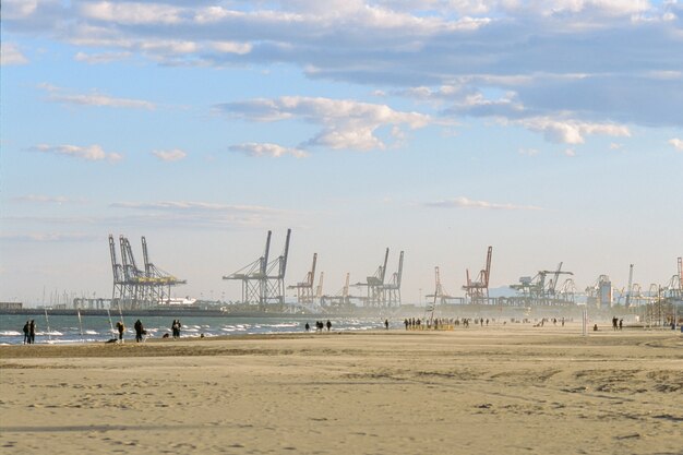 Leute, die auf den Strand von Valencia im Winter, Spanien gehen. Szene mit Industriehafen- und Containerkranen