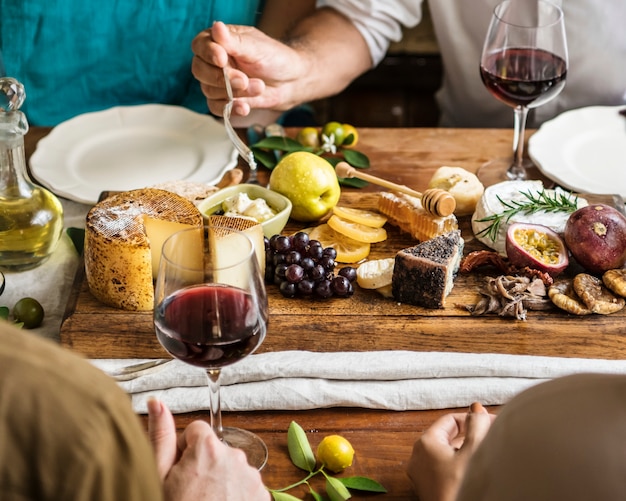 Leute, die eine Servierplatte des Käses mit Saisonfrüchten und Wein essen