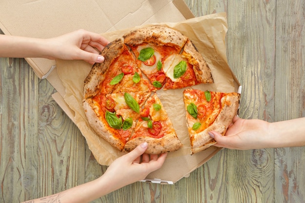 Leute, die Scheiben der köstlichen Pizza Margherita vom Tisch nehmen