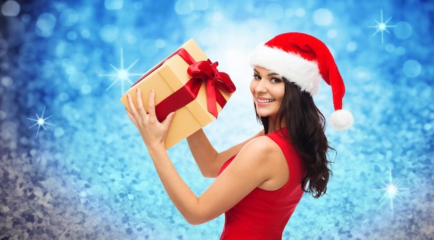 leute, feiertage, weihnachten und feierkonzept - schöne sexy frau in rotem kleid und weihnachtsmütze mit geschenkbox über blauem glitzer oder lichthintergrund