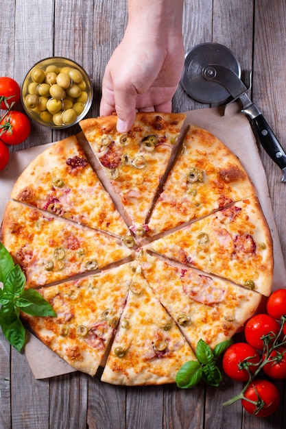 Foto leute hand, die scheiben der pizza nehmen. italienische pizza mit tomaten, mozzarella, oliven auf einem holztisch