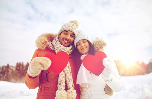 leute, jahreszeit, liebe und valentinstagkonzept - glückliches paar, das leere rote herzen über winterlandschaft hält
