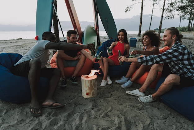 Leute stehen auf Strand um brennenden Klotz still.