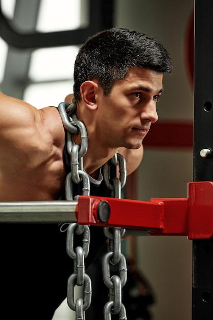 Levantador de pesas con una enorme cadena de metal alrededor del cuello Flexiones en las barras asimétricas del gimnasio