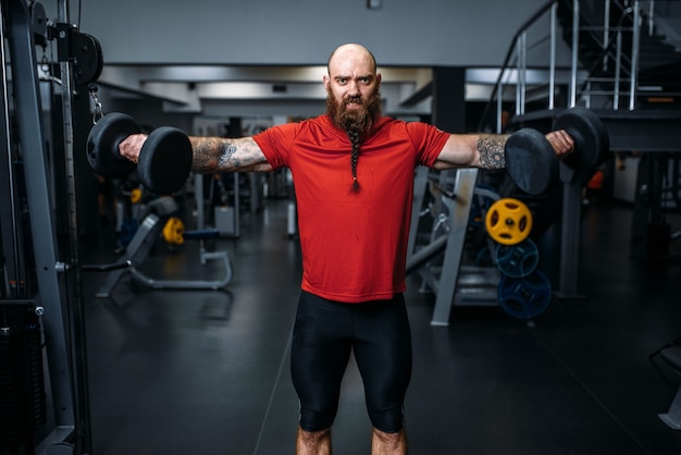 Levantador de pesas masculino fuerte haciendo ejercicio con pesas en el gimnasio.