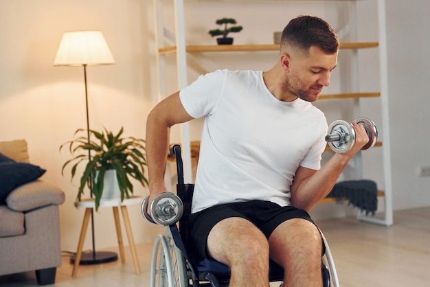 Levantando pesas El hombre discapacitado en silla de ruedas está en casa