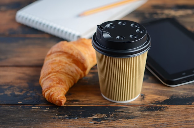 Leve embora o copo de café com o croissant na tabela de madeira.