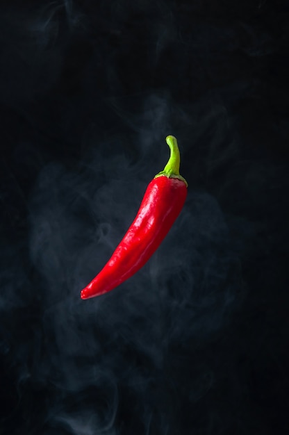 Levitación de ají rojo caliente en el aire con humo sobre fondo negro.