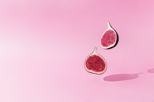 Levitación de mitades de fruta de higo sabroso fresco con sombra sobre fondo rosa. Dos secciones transversales de higo cayendo o volando. Concepto de desierto vegano. Sombra de volar alimentos saludables. Foto de alta calidad