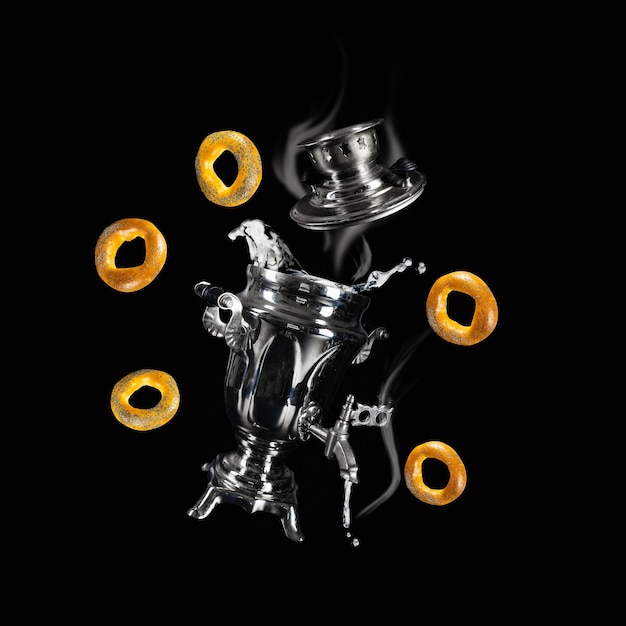 Levitando samovar com bagels e espirrando água quente com vapor em fundo preto