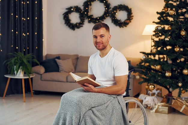 Leyendo el libro Se acerca el año nuevo El hombre discapacitado en silla de ruedas está en casa