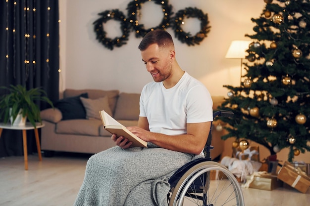 Leyendo el libro Se acerca el año nuevo El hombre discapacitado en silla de ruedas está en casa