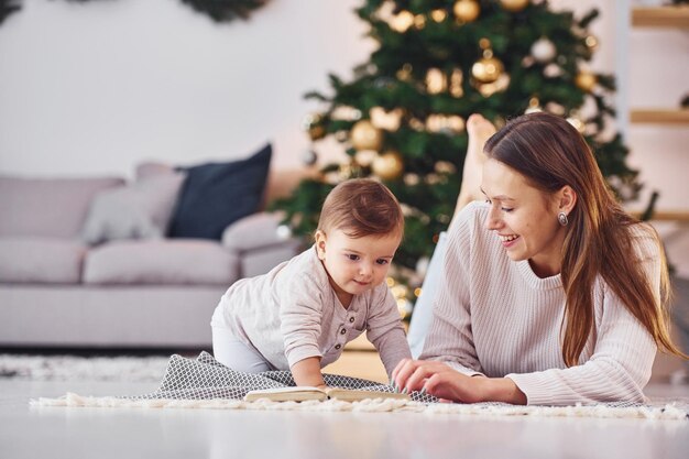 Leyendo un libro juntos Madre con su pequeña hija está adentro en casa juntos