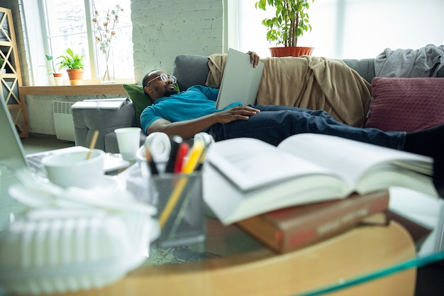 Leyendo libros, revistas. Hombre afroamericano que se queda en casa durante la cuarentena debido a la propagación del coronavirus, COVID-19. Tratando de pasar un tiempo útil y divertido. Concepto de salud y medicina.