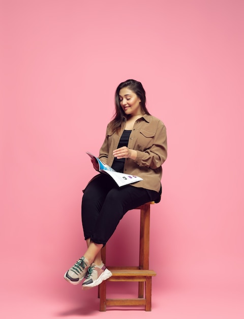 Leyendo la revista. Mujer joven en ropa casual sobre fondo rosa. Carácter corporal positivo, feminismo, amarse a sí misma, concepto de belleza. Plus size empresaria, hermosa niña. Inclusión, diversidad.