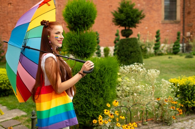 LGBT-Flagge auf ihrem Gesicht, das mit Regenbogenregenschirm aufwirft