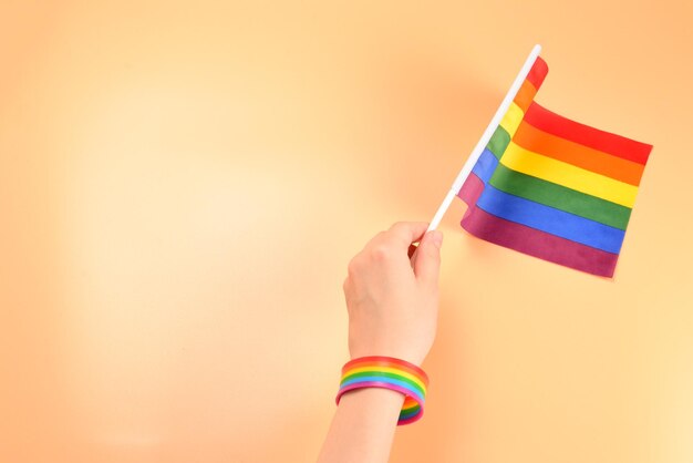 LGBT-Flagge in der Hand der Frau auf orangefarbenem Hintergrund Platz kopieren