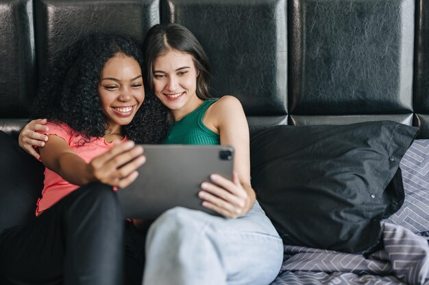 Foto lgbt-frauen sitzen auf dem bett und schauen tablet-bildschirm glücklich lächelnd zusammen zu hause urlaubsaktivität