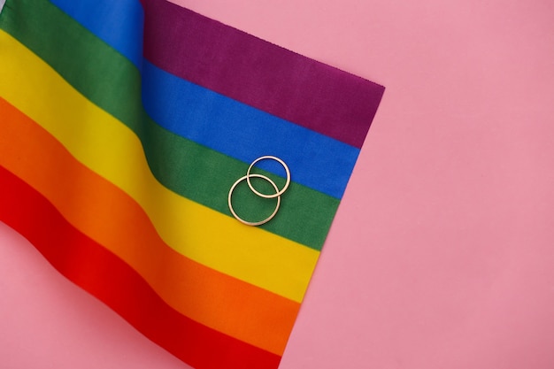 LGBT-Hochzeit. LGBT-Regenbogenflagge und goldene Ringe auf rosa Hintergrund. Toleranz, Freiheit