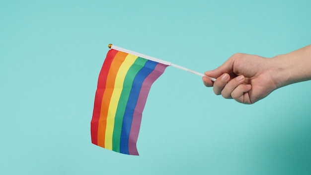 LGBT-Konzept. Hand hält eine Regenbogenflagge auf mintgrünem oder tiffanyblauem Hintergrund.