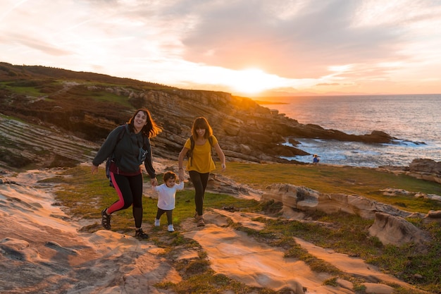 Lgbt-paar frauen mit einem kind bei sonnenuntergang an der küste am meer familienlebensstil