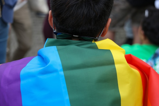 LGBT-Regenbogenflagge bedeckt an zurück von einem Mann, der in Parade geht.