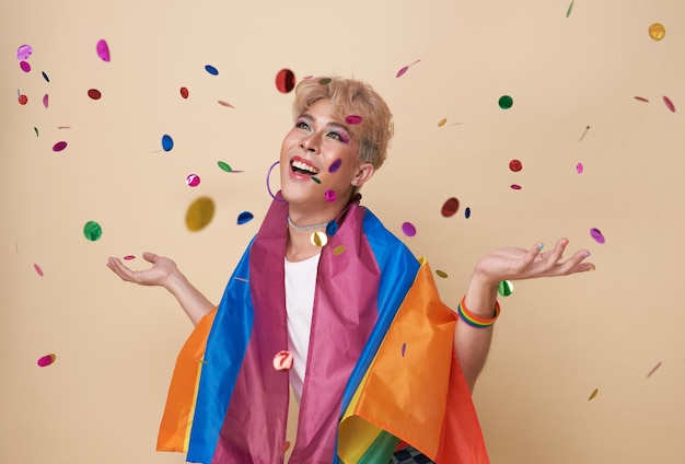 LGBT transgénero asiático celebra y confeti con la bandera del arco iris aislada sobre fondo de color desnudo