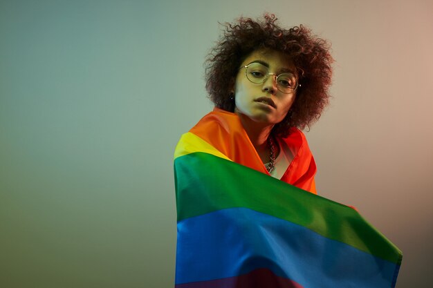 Lgbtq-Konzept. Positives kaukasisches Mädchen mit Afro-lockigem Haar, das Regenbogenfahne lokalisiert hält