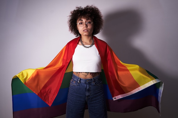 Lgbtq-Konzept. Positives kaukasisches Mädchen mit Afro-lockigem Haar, das Regenbogenfahne lokalisiert im Studio hält