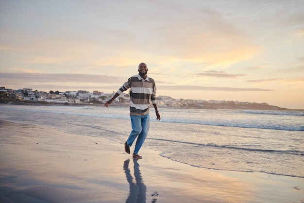 Liberdade de praia e férias com um homem negro à beira-mar ou mar correndo na areia com uma vista do pôr do sol do céu Natureza água e verão com um jovem macho desfrutando de férias na costa