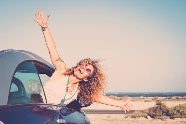 Liberdade e viagens felizes rindo conceito de pessoas com bela jovem caucasiana fora do carro apreciando o local de destino abrindo os braços e gritando de graça